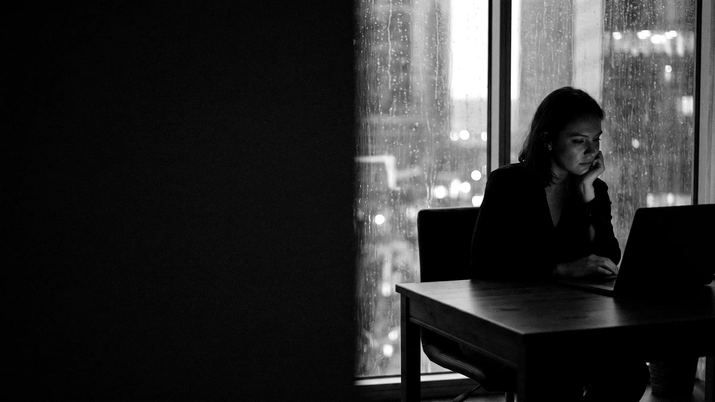 A woman working late at a laptop in a dark apartment